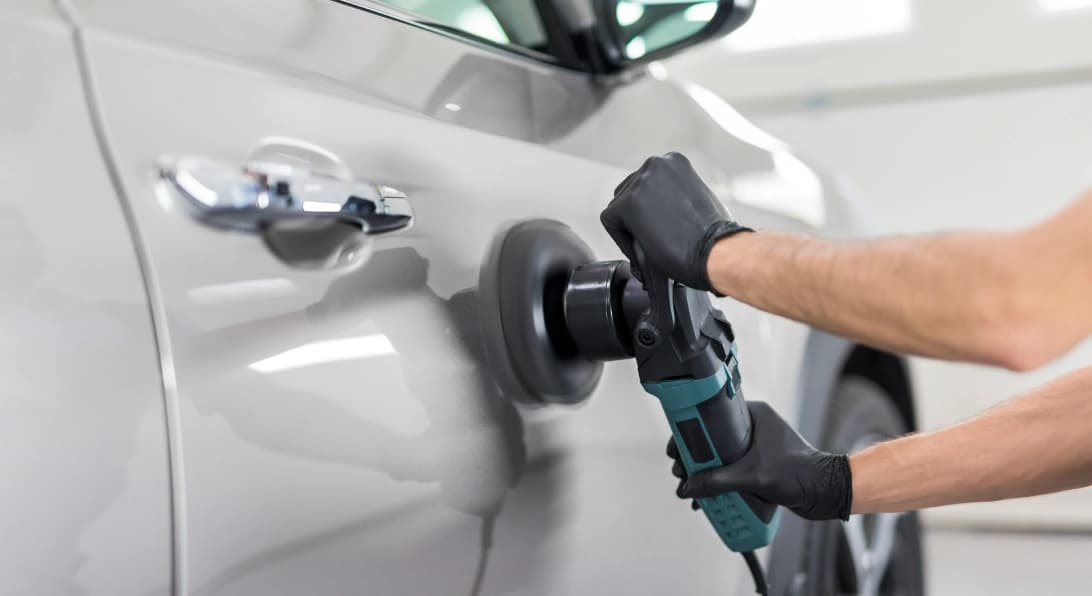 Pessoa utiliza ferramenta especializada para polir a porta de um veículo.